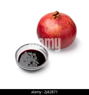 Single glass bowl with pomegranate sauce and a single whole pomegranate  isolated on white background Stock Photo