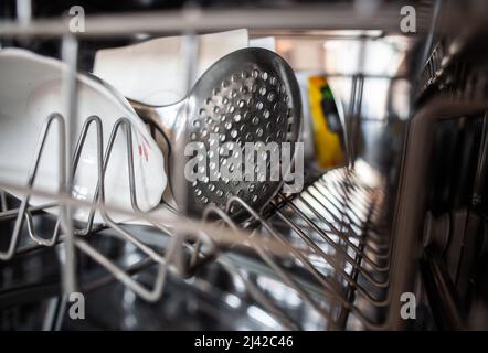 Close up of dirty dishes on upper rack in dishwasher Colander in dishwasher, with colorful yellow mug, white plate and bowl Stock Photo