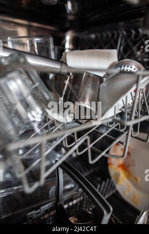 Close up of dirty dishes on upper rack in dishwasher Tea strainer with tea leaves leftovers in dishwasher, glasses, colander, plates, bowl, basket Stock Photo