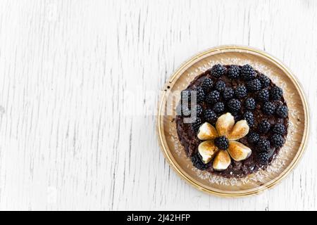 Raw vegan rich dark chocolate cake on a white table. Minimalism food photography concept. The cake decorated with blackberries and cuted fig. Copy spa Stock Photo