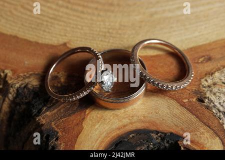White Gold and Diamond Wedding and Engagement Rings Arranged on Rustic Wood Tree Slice Stock Photo