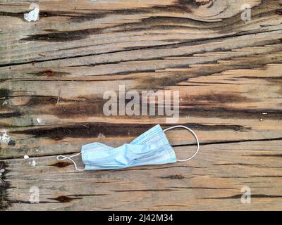 Used disposable paper face mask on weathered wooden floor Stock Photo
