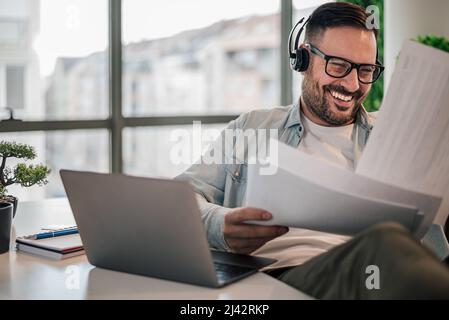 Delighted adult man, inspecting the files while listening to music on his headphones. Stock Photo