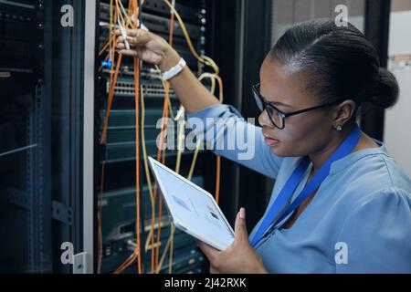 Everything seems okay.... Cropped shot of an attractive female programmer working on a tablet in a server room. Stock Photo