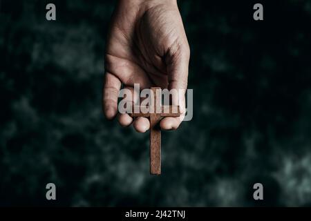 a man is holding a wooden cross in his hand, on a black mottled background Stock Photo