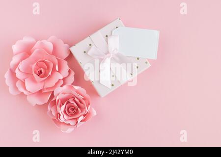 Paper roses with gift box and blank card with message space on pink background. Copy space. Stock Photo