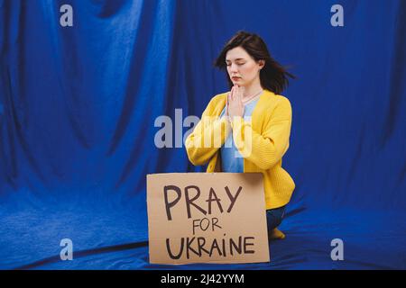 A Ukrainian woman in a yellow jacket and blue jeans with a sign Pray for Ukraine. Ukrainian girl suffered from the war. There is no war. A woman prote Stock Photo