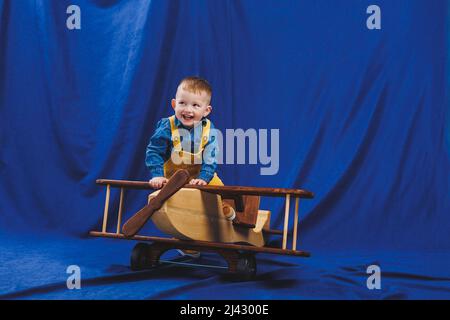 A 3-year-old boy in a checkered shirt sits on a large wooden plane. Children's environmentally friendly toys from wood Stock Photo