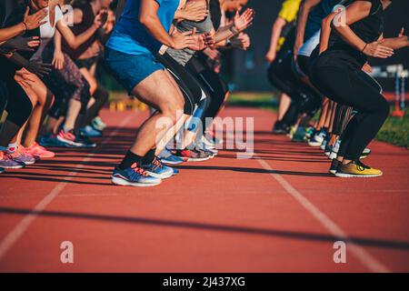 Team training outdoors on an athletic track. Group warm-up before the run. Stretching and strengthening before training. Group sports for motivation a Stock Photo
