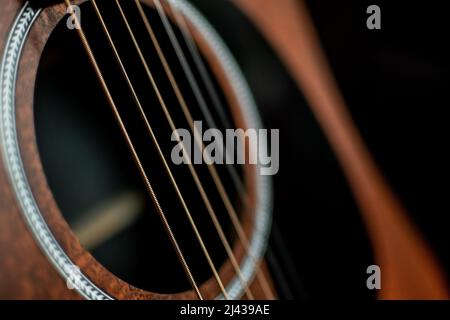 An angled close-up view of the sound hole and steel strings of an acoustic guitar. Stock Photo