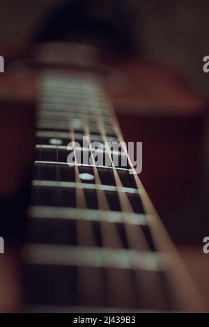 Close up view looking down the neck of a guitar showing the fretboard with multiple frets and position markers with the guitar body in the background Stock Photo
