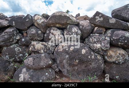 Ancient wall of round dark rocks with sky behind Stock Photo