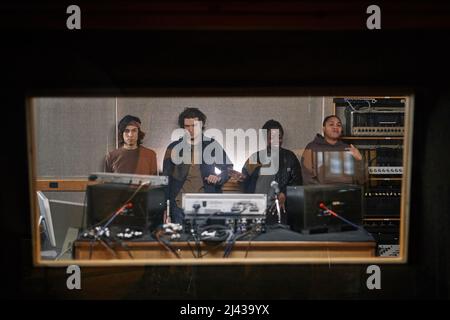Graphic portrait of diverse music band composing new album in professional recording studio behind glass wall Stock Photo