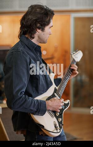 Vertical portrait of handsome young man playing electric guitar in recording studio and composing new music Stock Photo