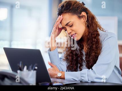 Its a little daunting. Cropped shot of an attractive young businesswoman suffering with a headache while working on her laptop in the office. Stock Photo