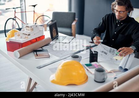 Proper planning saves you precious time, especially in this profession. Shot of a handsome young architect working on building plans and designs in Stock Photo