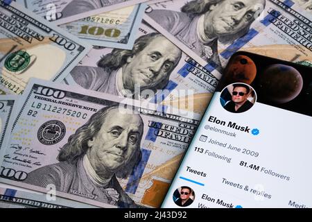 Official Elon Musk's twitter account page seen on the smartphone which is placed on the pile of dollar banknotes. Concept. Selective focus. Stafford, Stock Photo