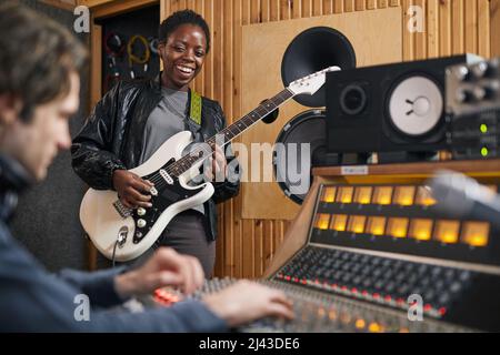 Portrait of black young woman playing electric guitar while composing music in professional recording studio, copy space Stock Photo