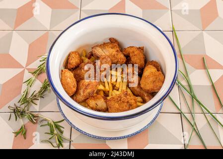 Fried chicken pieces with potatoes and rosemary in a deep enamel bowl Stock Photo