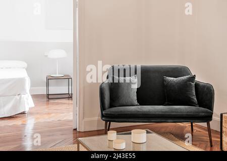 Decorative details of a living room with a dark green velvet upholstered armchair and access to a bedroom with white bedding Stock Photo