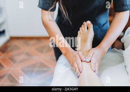 Unrecognizable therapist making a foot and leg massage to a female patient. Wellness center spa. Foot care. Stock Photo