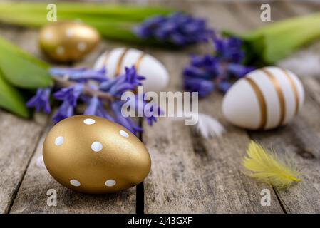 Golden-white Easter eggs with feathers and blue hyacinths on a rustic wooden table. Easter concept. Stock Photo