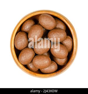 Milk chocolate Easter eggs, in a wooden bowl. Mini chocolate eggs, a sweet candy. Isolated, from above, on white background, macro food photo. Stock Photo