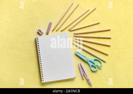 Colorful pencils, blank notebook and stationery on yellow grunge background Stock Photo