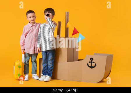 Funny little boys playing with cardboard ship on yellow background Stock Photo