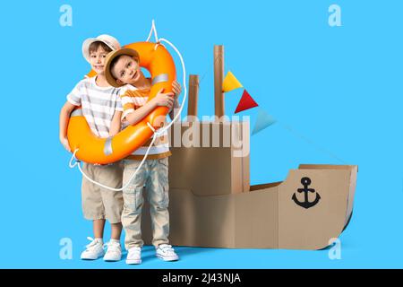 Funny little boys playing with cardboard ship and lifebuoy on blue background Stock Photo