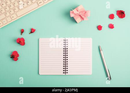 Blank notepad with pen, computer keyboard. gift box and red spring flowers on teal blue background. Top view, flat lay. Stock Photo