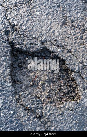 Pot hole in asphalt road. Damaged highway with hole in it. Dangerous holes to be repaired after winter . Stock Photo