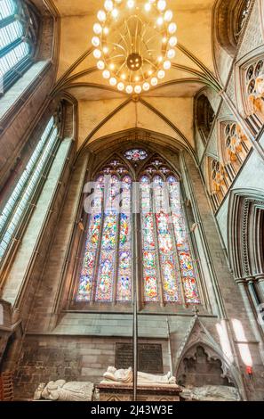 Low angle view of majestic,colorful ornate windows,and hanging ceiling lightis,overlooking the isle and memorial tombs inside the cathedral church of Stock Photo