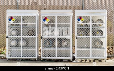 Liquid Petroleum gas cylinders stored horizontally in a metal safety cage with NFPA warning signs on the closed doors, front view outside. Stock Photo