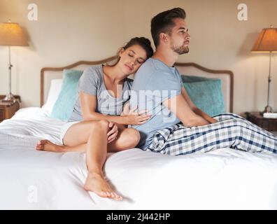 Shes having a hard time trying to cheer him up. Shot of a young couple having an argument in their bedroom at home. Stock Photo