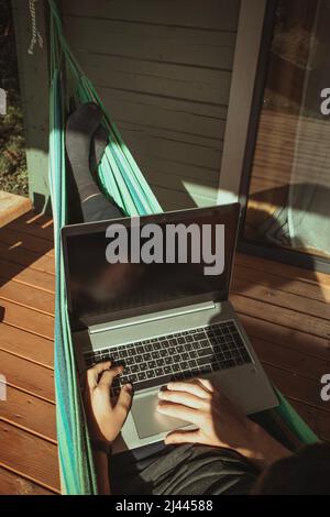 A top view of man working in hammock near cottage. Distant work, freelancer Stock Photo
