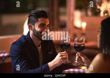To a fine night out. Shot of a cheerful young couple having a celebratory toast with wine glasses while looking into each others eyes over dinner Stock Photo