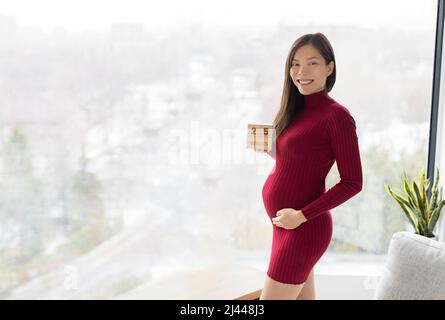 Pregnant woman showing 25 weeks pregnancy bump for maternity photoshoot holding wooden blocks sign happy. Asian beautiful model happy standing at home Stock Photo