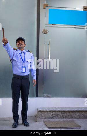 Security guard pointing away with stick while working in front of gate Stock Photo