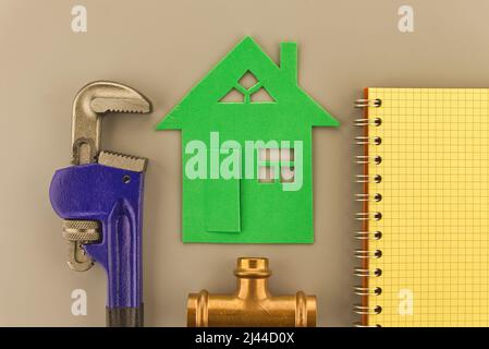 DIY, renovation or new build home concept with wrench, copper plumbing joint and notebook alongside a spiral bound notebook and green cutout of a hous Stock Photo