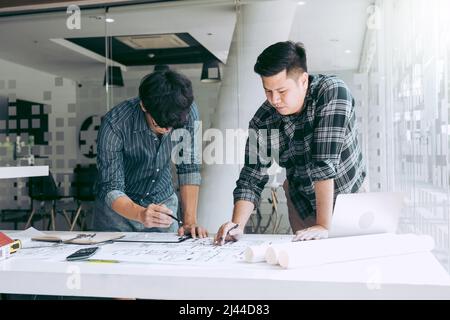 Architects or engineering working with blueprints and discussing project together at the meeting in the office. Stock Photo
