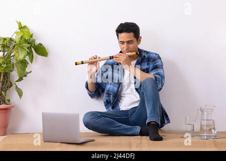 Young music teacher playing flute during online class in living room Stock Photo