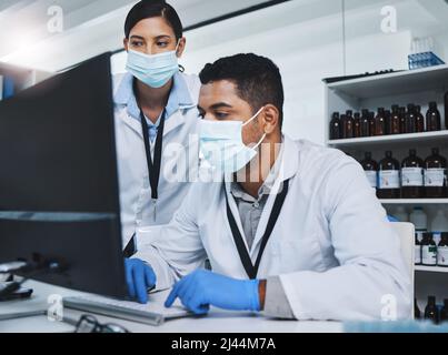 Every contribution brings us closer to our goal. Shot of two young researchers using a computer in a laboratory. Stock Photo