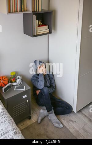 Depressed male teenager sitting on the floor in his bedroom Stock Photo