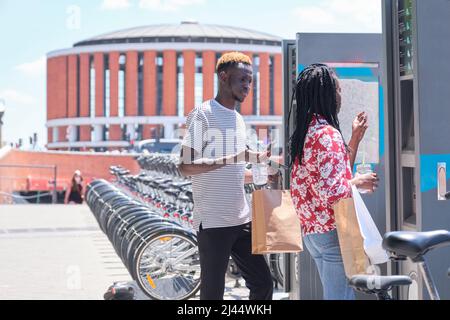 Young african tourists renting a bike at a bicycle rental service machine. Stock Photo