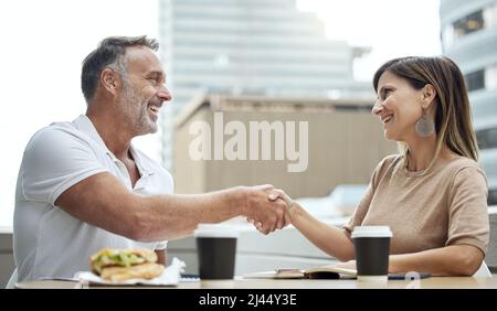 Business meetings made better over lunch. Shot of two businesspeople shaking hands while having lunch outside an office. Stock Photo