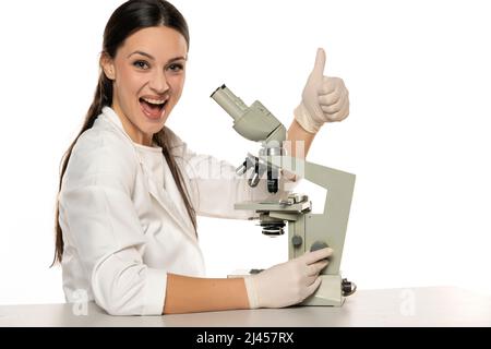 Portrait of happy female scientist with microscope, showing thumbs up on a white background Stock Photo