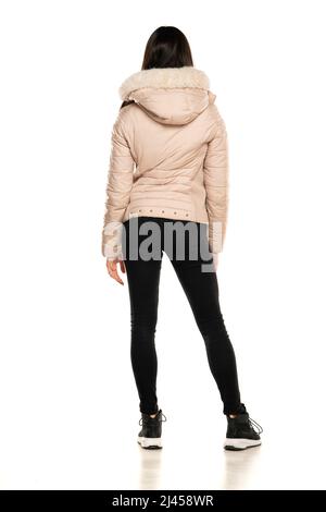 Rear view of a young woman in winter jacket, and black jeans posing on a white background Stock Photo