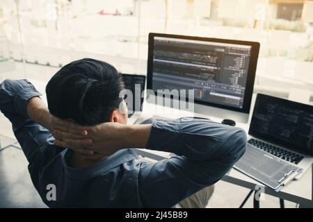 Asian programmers man are relaxing and looking at the code on the computer screen in the office. Stock Photo