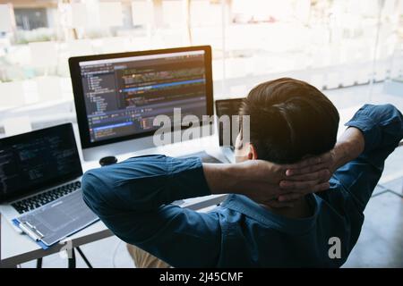 Asian programmers man are relaxing and looking at the code on the computer screen in the office. Stock Photo